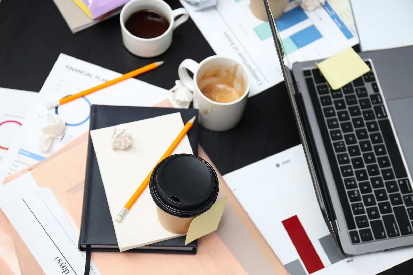 Scrivania d'ufficio con portatile, documenti, appunti e tazze di caffè