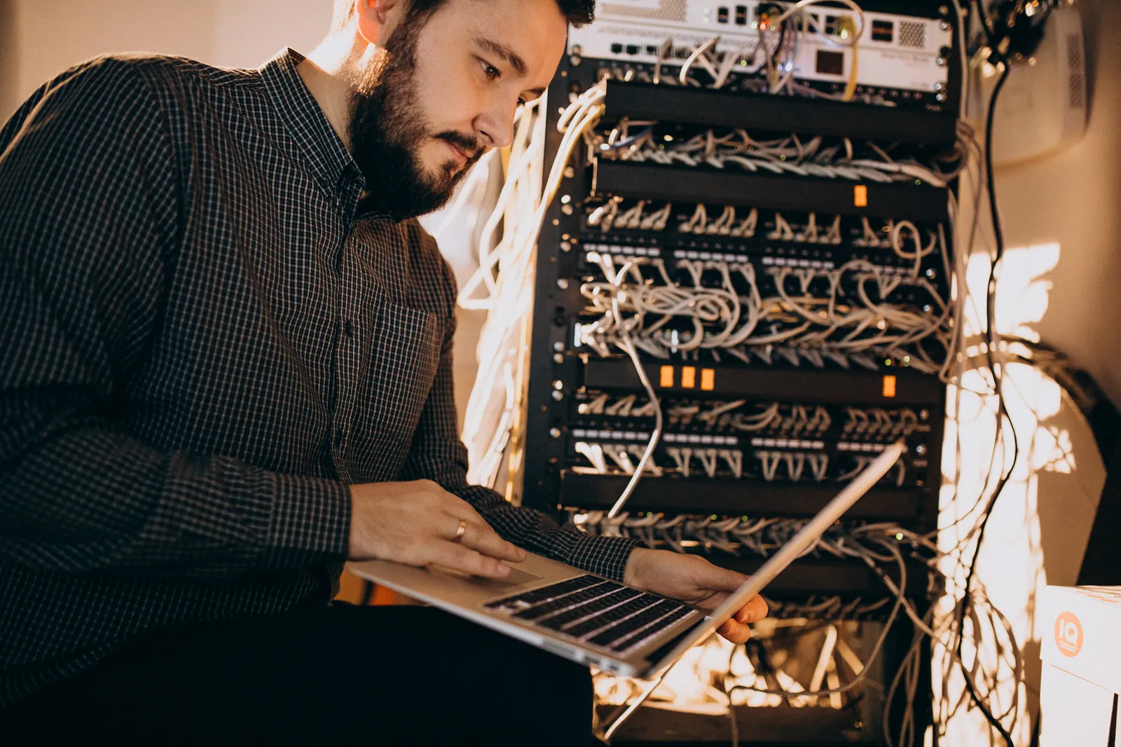 Tecnico con il portatile collegato a un piccolo armadio di rete aziendale con switch e cavi