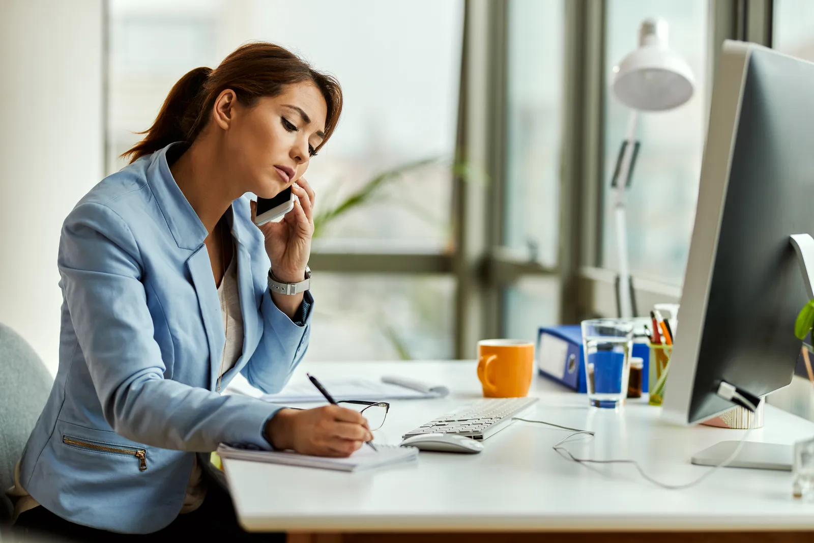 Impiegata amministrativa al telefono che prende appunti alla scrivania